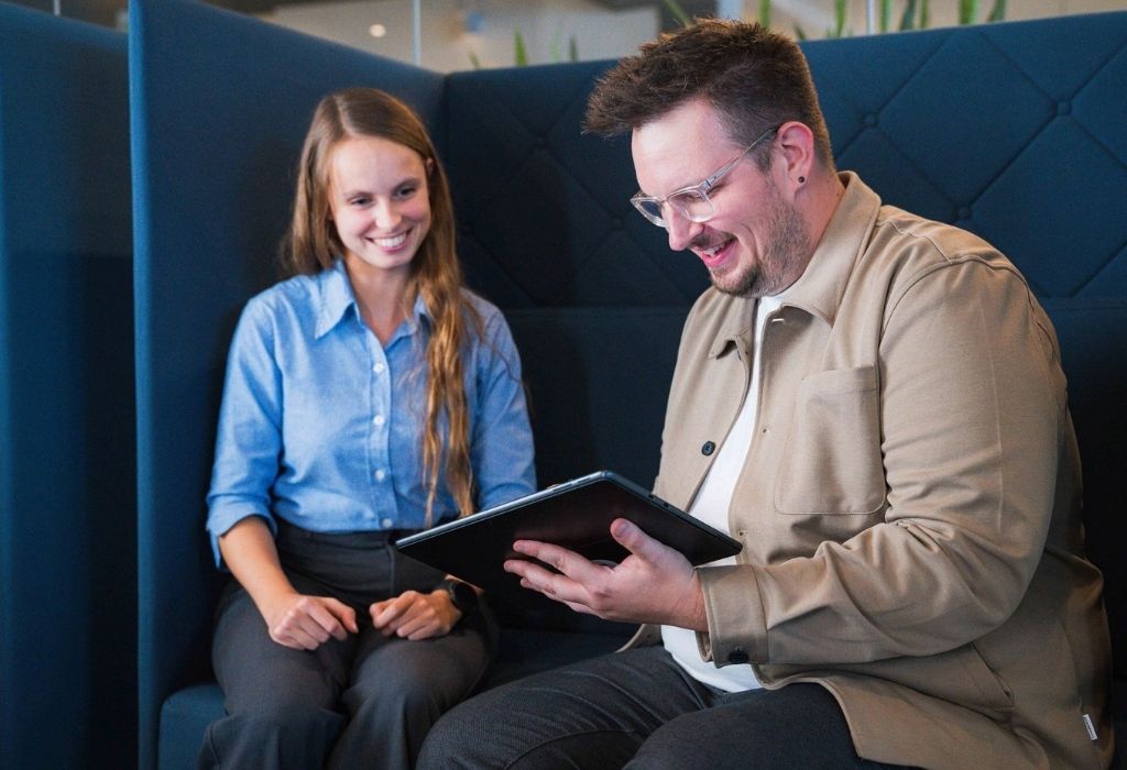 Zwei Personen sitzen in einer gemütlichen Sitznische und schauen gemeinsam auf ein Tablet.