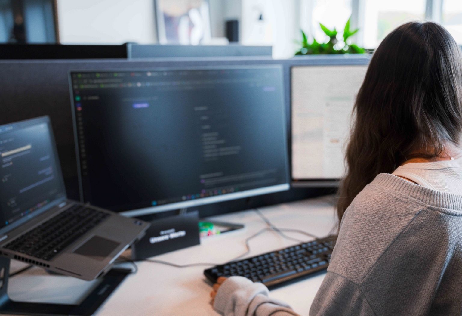 Eine Frau sitzt an einem Schreibtisch mit zwei Monitoren und arbeitet konzentriert an ihrem Computer.