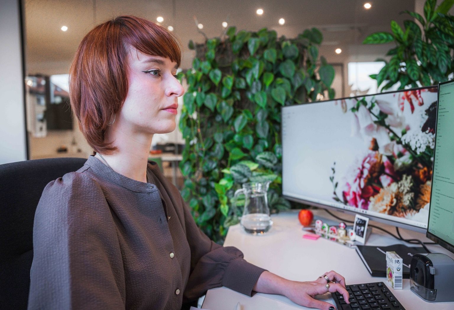 Eine Frau arbeitet an einem Computer an ihrem Schreibtisch, neben ihr steht eine Pflanze.