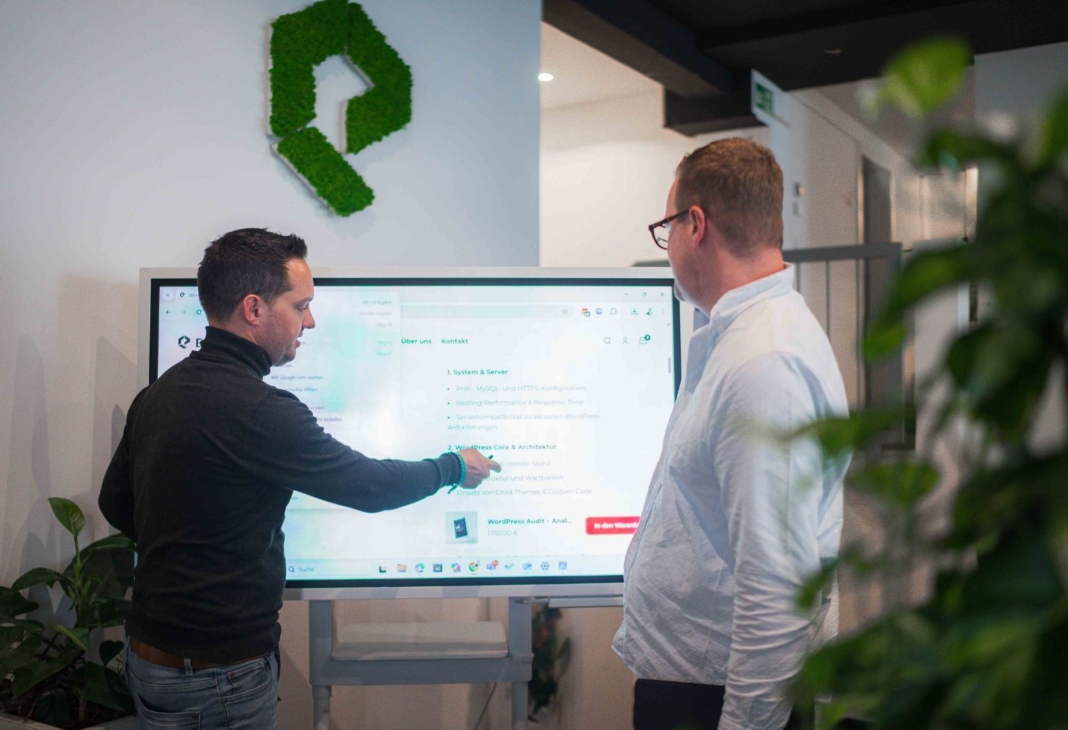 Zwei Männer stehen vor einem großen Bildschirm und diskutieren über digitale Strategien.